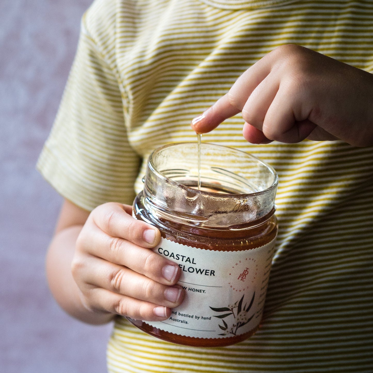 Child dips finger in jar of western Australian premium honey jar has label from The Rare Honey Company Coastal Wildflower